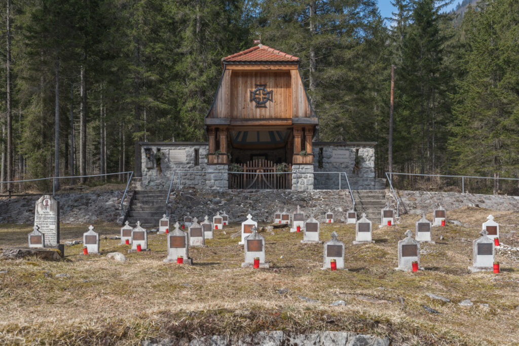 Austro-węgierski cmentarz wojenny Heldenfriedhof z I wojny światowej w Valbrunie, otoczony lasem. Widok na rzędy grobów i drewnianą kaplicę.